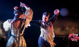 Dos bailarinas de flamenco, con trajes de lunares y flecos, interpretan apasionadas canciones de sevillanas bajo luces de escenario.