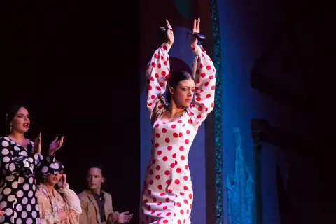 Bailarina de flamenco andaluz con vestido de lunares rojos, castañuelas en alto.