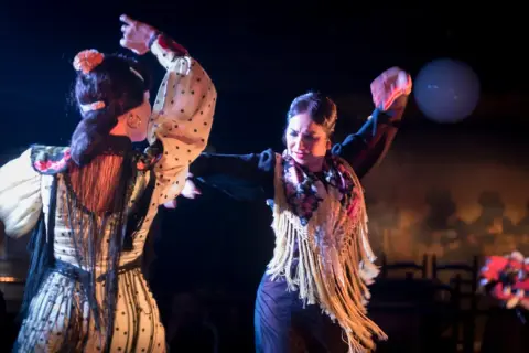 Dos mujeres bailan flamenco, el baile típico de España, con pasión y gracia. Sus trajes vibrantes y movimientos expresivos capturan la esencia de esta arte.