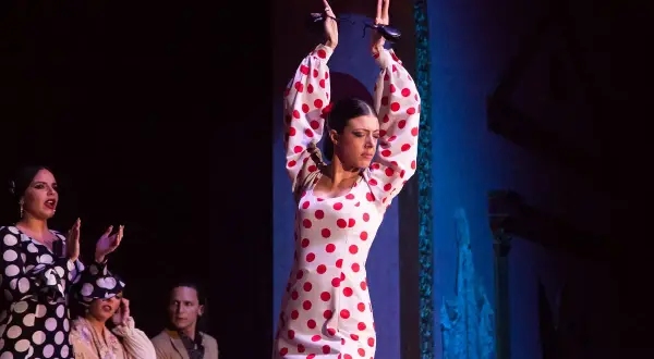 Bailarina de flamenco andaluz con vestido de lunares rojos, castañuelas en alto.