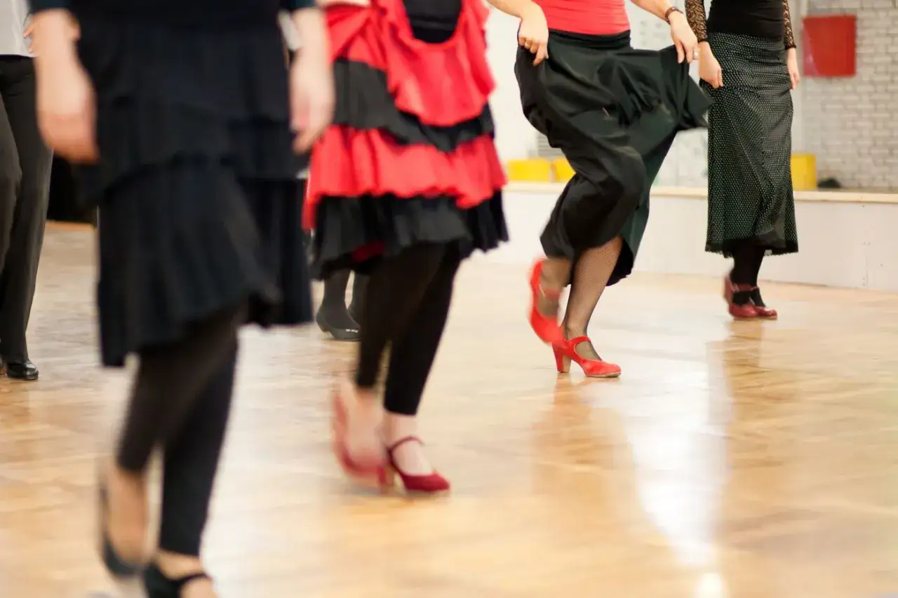 Personas en movimiento durante clases de flamenco para adultos. Se ven faldas amplias y zapatos de tacón.