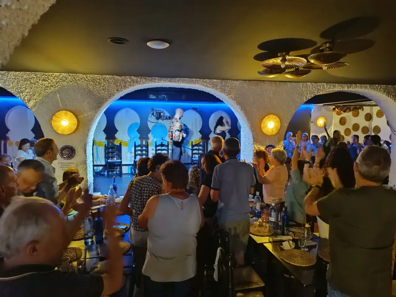 Un p&uacute;blico aplaude con entusiasmo en un tablao flamenco. El artista en el escenario recibe un 