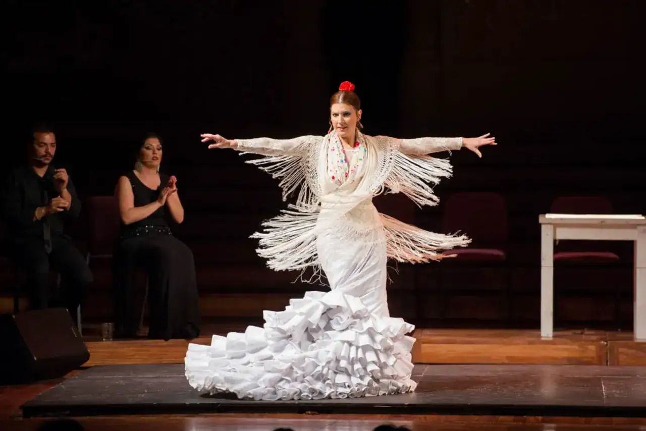 Bailaora de flamenco con vestido blanco y mant&oacute;n de flecos, capturando el significado del flamenco en su expresi&oacute;n.