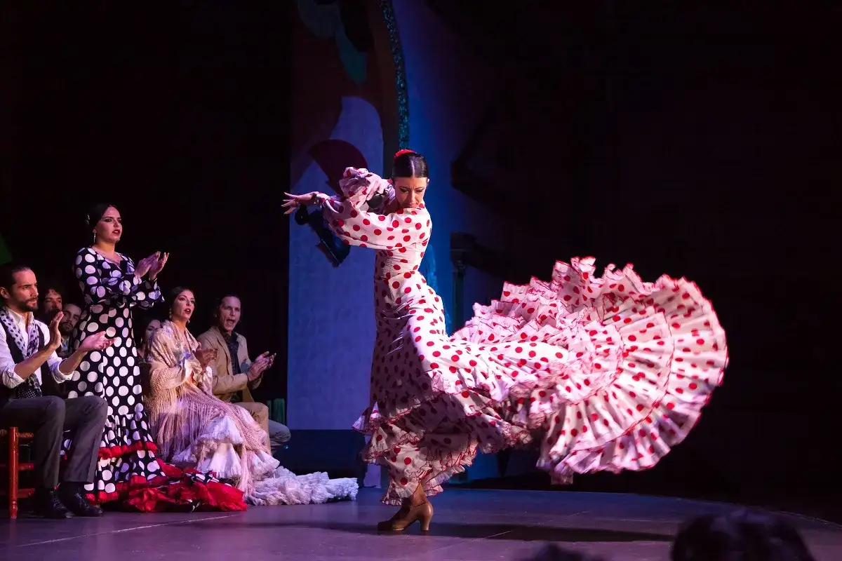 Una bailaora de flamenco, con un vestido de lunares rojos y blancos, despliega su falda en un giro apasionado. El p&uacute;blico aplaude la seguidilla.