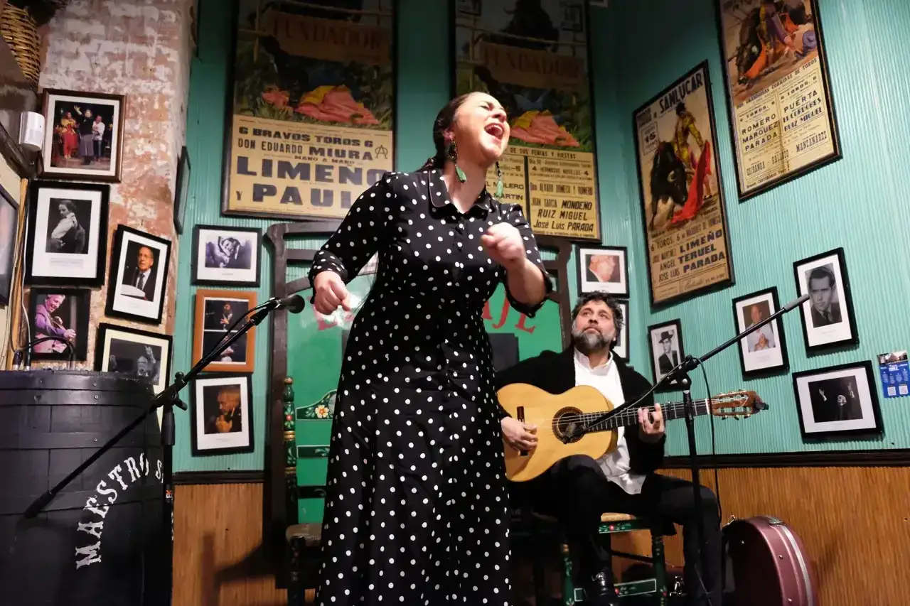 Una mujer canta con pasi&oacute;n, capturando las expresiones jerezanas, mientras un guitarrista la acompa&ntilde;a en un escenario &iacute;ntimo.