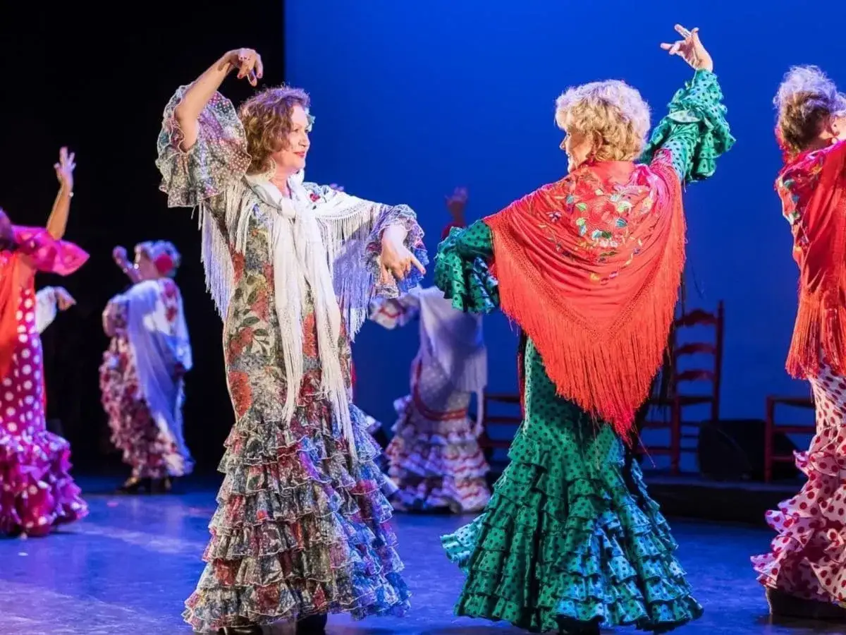 Dos mujeres bailan un baile t&iacute;pico de Andaluc&iacute;a con vestidos flamencos coloridos y mantones bordados.