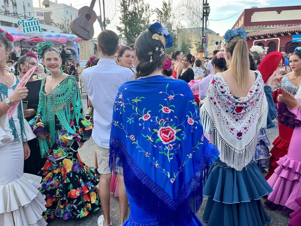 Mujeres con trajes de flamenca y mantones bordados, uno azul con flores rojas y otro blanco con bordados coloridos.