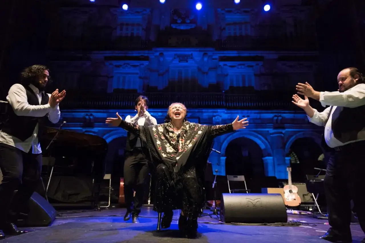 La Chana, ic&oacute;nica bailaora flamenca, canta con pasi&oacute;n en el escenario, rodeada de m&uacute;sicos.
