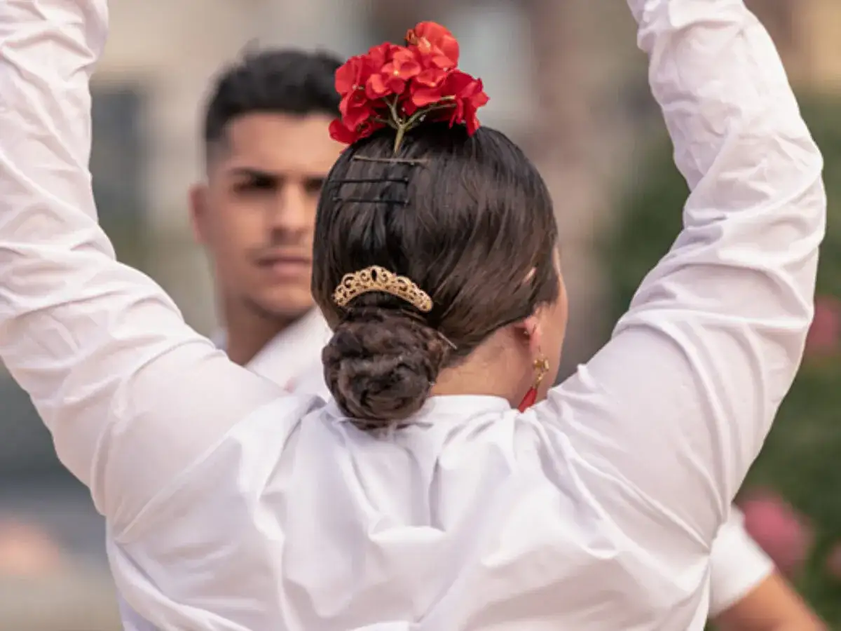 Peinados para bailar flamenco: moño recogido con flor roja y adorno dorado. Un hombre al fondo.
