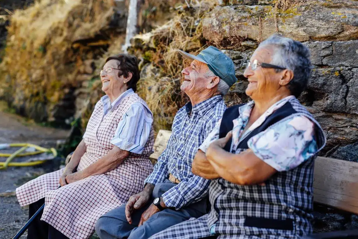 Tres ancianos sonr&iacute;en sentados en un banco, sus expresiones reflejan la alegr&iacute;a de las expresiones sevillanas.