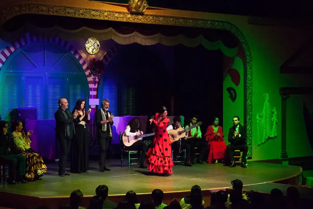 Una bailarina de tango flamenco con vestido rojo y lunares negros cautiva en el escenario, acompa&ntilde;ada por guitarristas y cantantes.