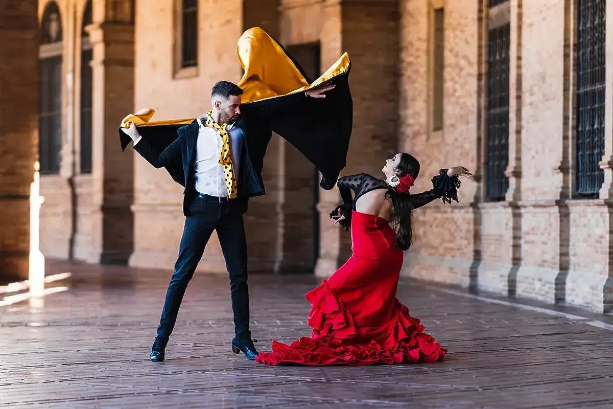 Pareja bailando flamenco, ella con vestido rojo, &eacute;l con capa. El jaleo significado se siente en su pasi&oacute;n.
