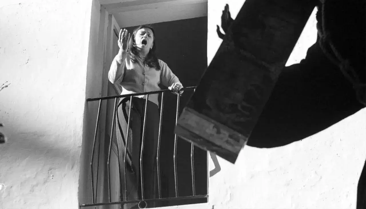 Mujer en balc&oacute;n, con la boca abierta, parece cantar o gritar, quiz&aacute;s una de las saetas populares que resuenan en la calle.