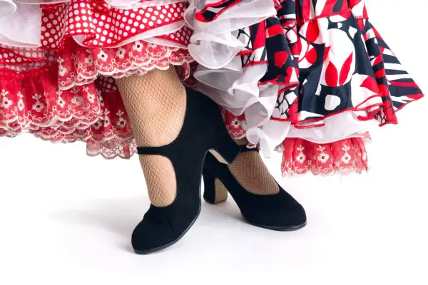 Zapatos negros de tacón y medias de rejilla, listos para el zapateo flamenco entre volantes de lunares y encaje.